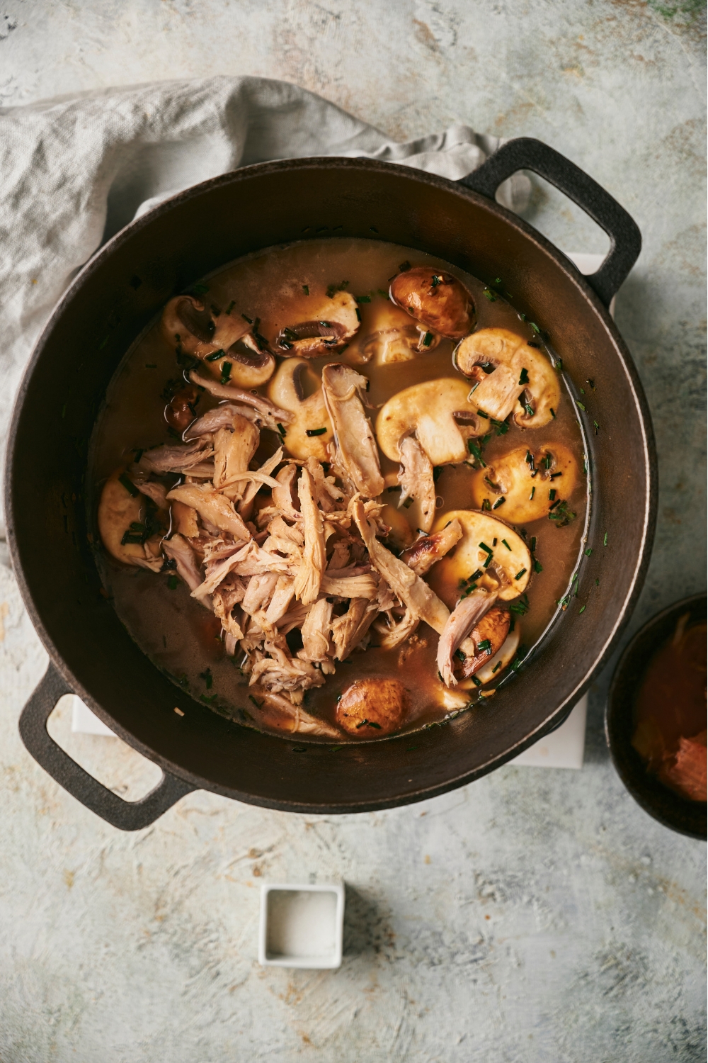 A black Dutch oven filled with mushroom slices, shredded chicken, and broth.