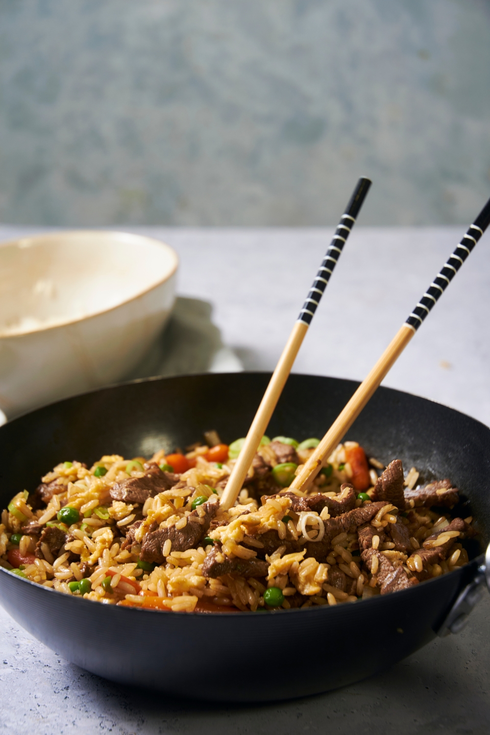 A black bowl of beef fried rice with chopsticks in the bowl.