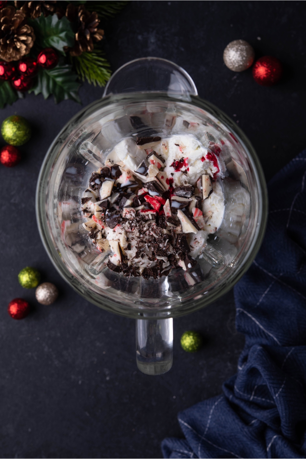 Blender filled with ice cream and peppermint bark, surrounded by Christmas ornaments.