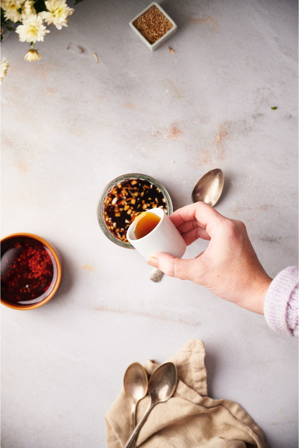 A hand pouring sesame oil into a clear bowl of soy sauce and garlic.