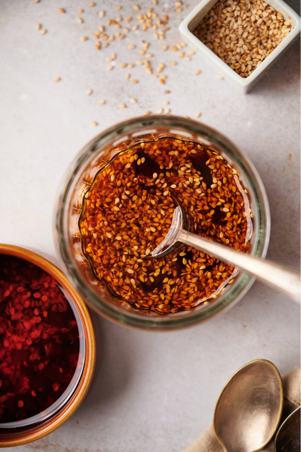 A clear bowl of dumpling sauce next to bowls of sesame seeds and chili oil.