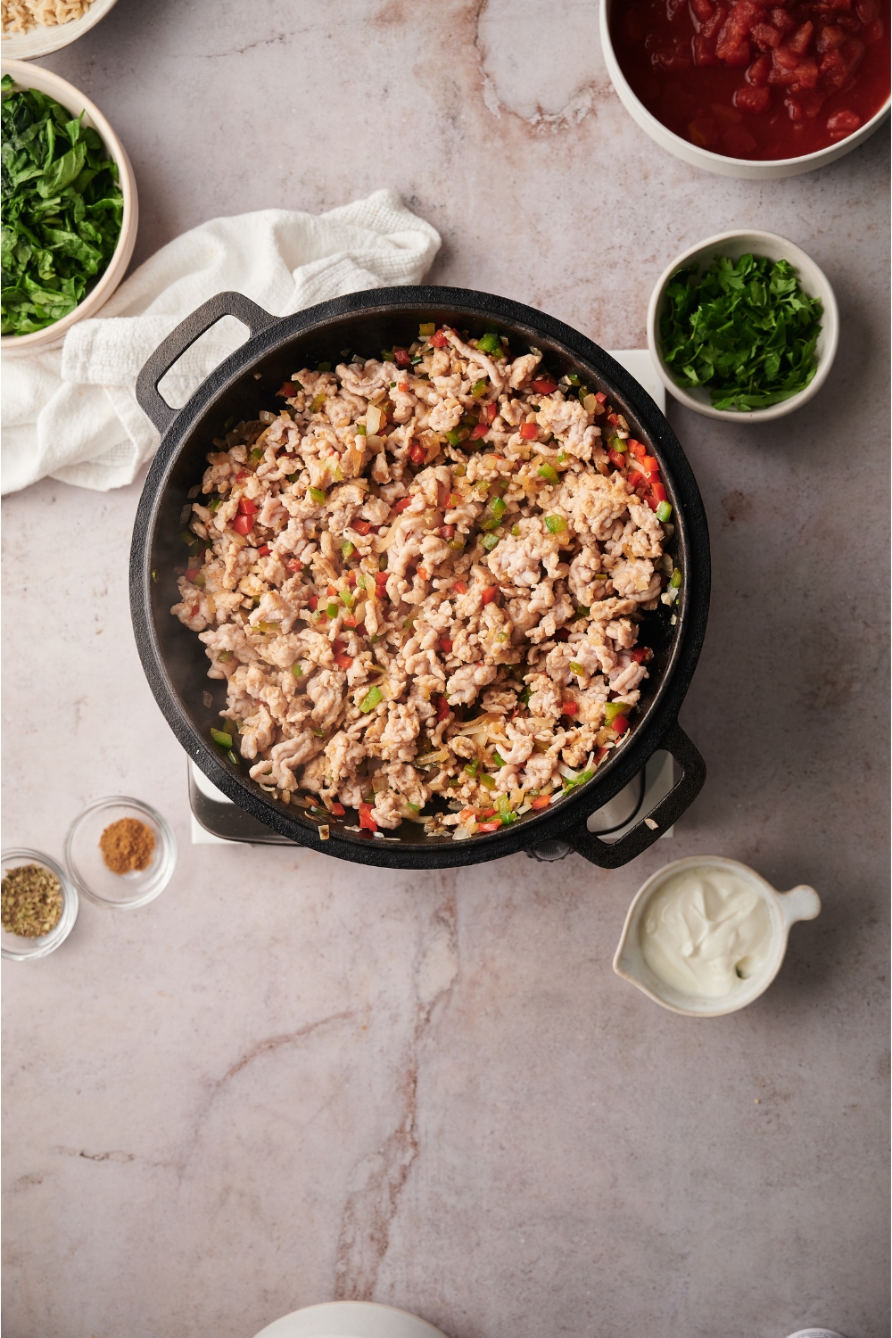 Black skillet filled with cooked ground turkey, diced peppers and diced onions. The skillet is surrounded by an assortment of ingredients.