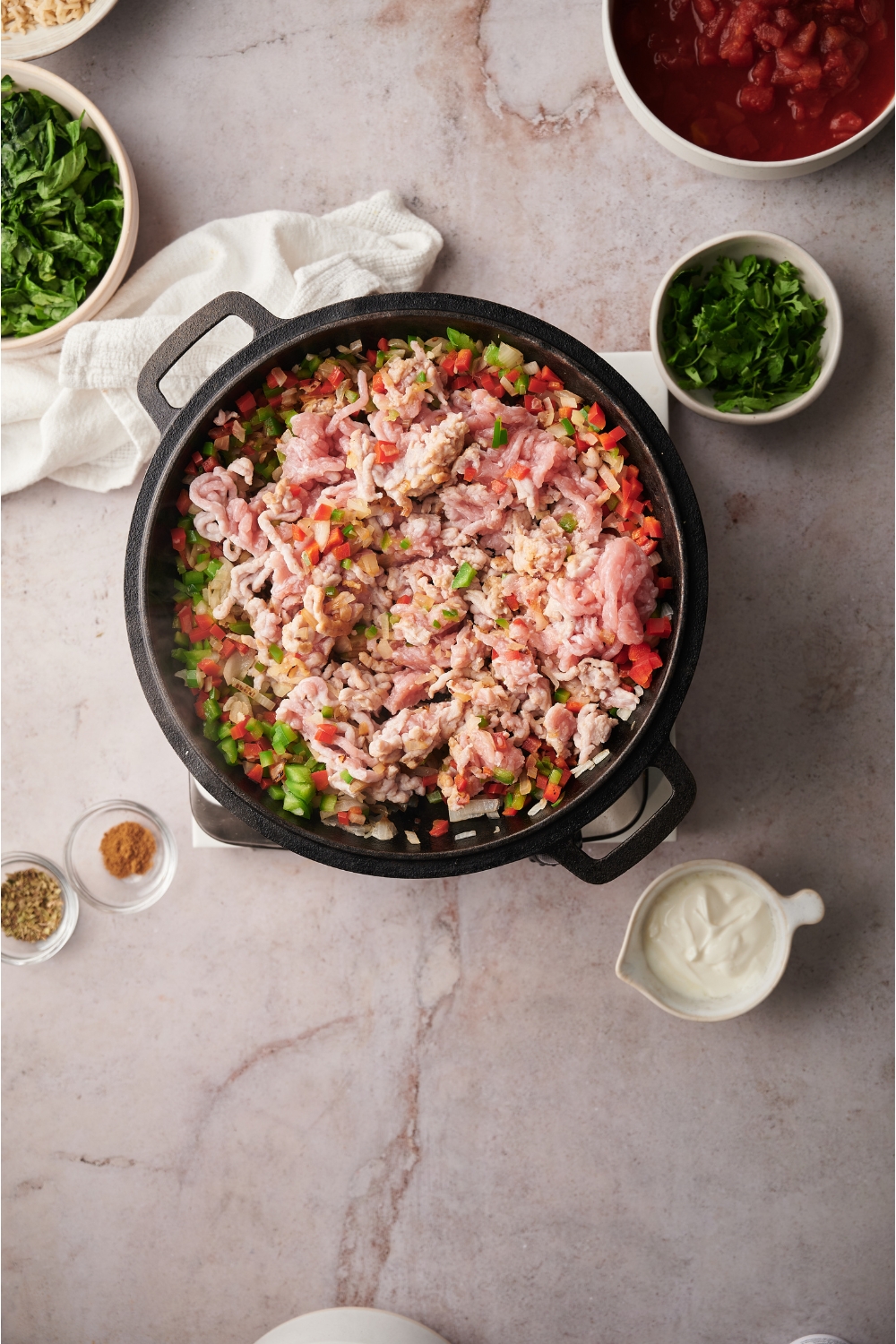 Black skillet filled with raw ground turkey, diced peppers and diced onions. The skillet is surrounded by an assortment of ingredients.