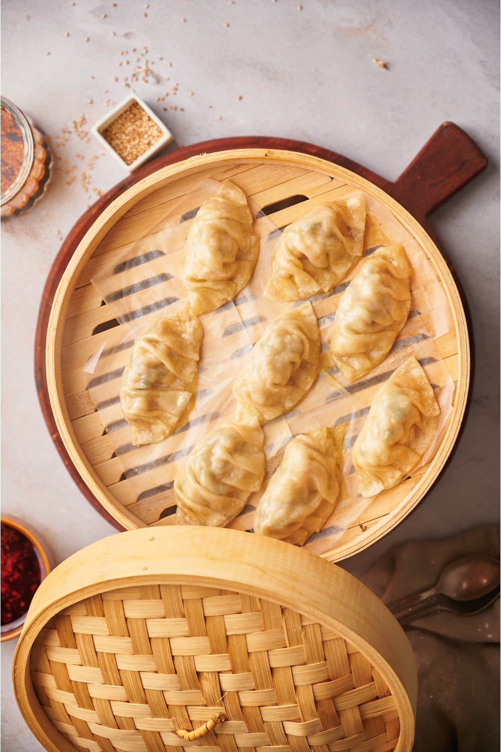 Steamed dumplings in a bamboo steamer resting on a wood board. The lid has been removed and is balanced on the side of the steamer.
