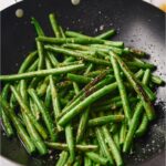 Cooked and seasoned green beans in a black skillet.