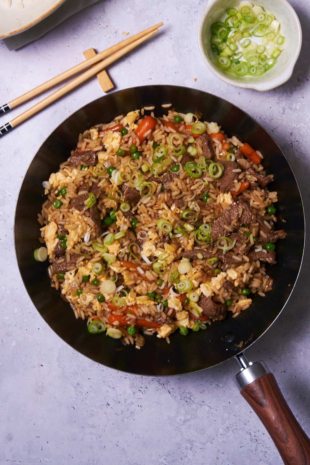 A black skillet filled with rice, peas, carrots, cooked beef, and green onions.