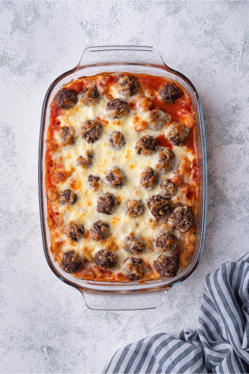 A clear baking dish with pasta, red sauce, meatballs, and melted cheese.