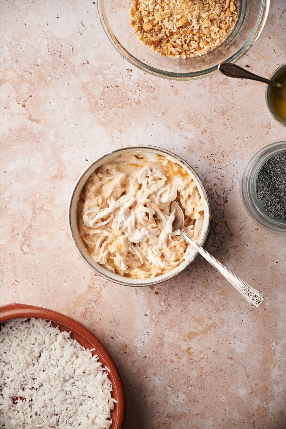 A white bowl with shredded chicken in a creamy mixture with a spoon in the bowl.