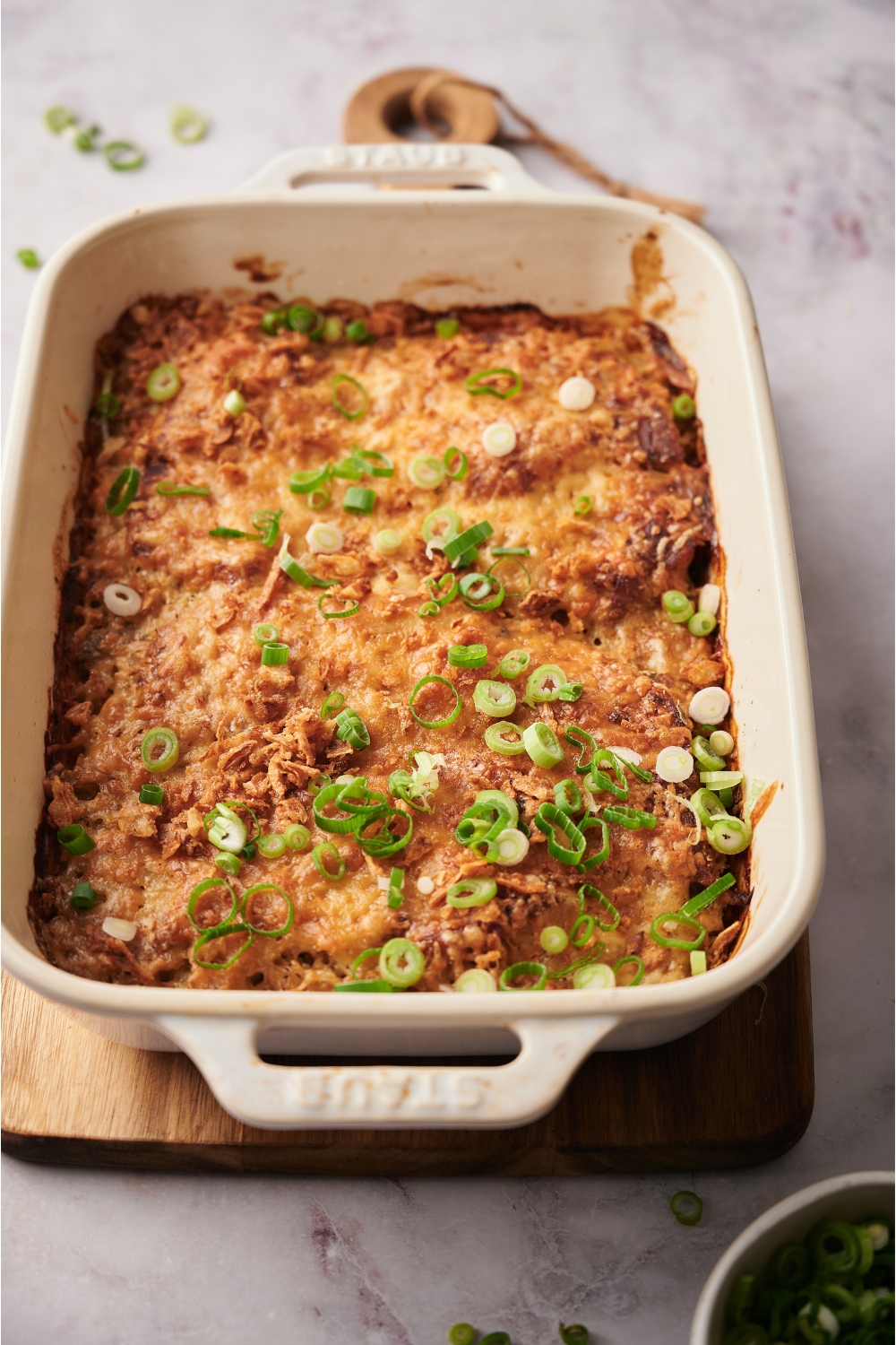 Green onions garnished on a freshly baked casserole in a white casserole dish that is on top of a wood board.