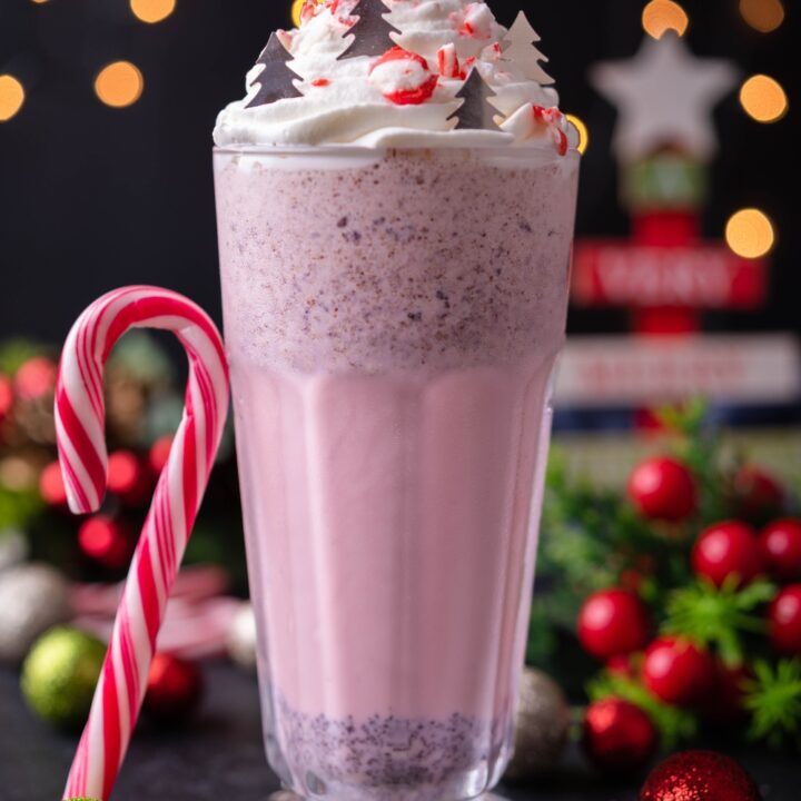 Peppermint milkshake topped with whipped cream, crushed candy cane, and chocolate Christmas trees, with a candy cane propped against the milkshake.