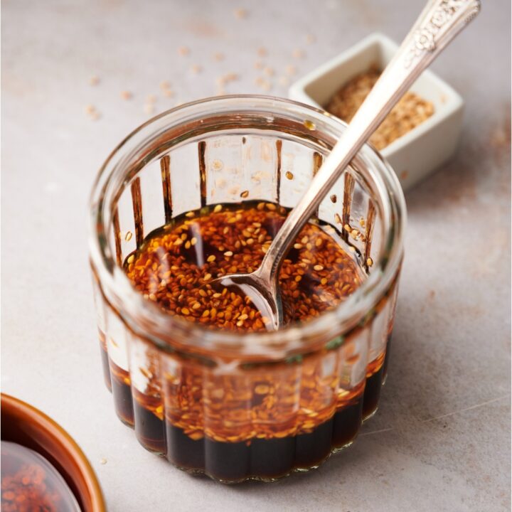 A clear jar containing dumpling sauce and a spoon.