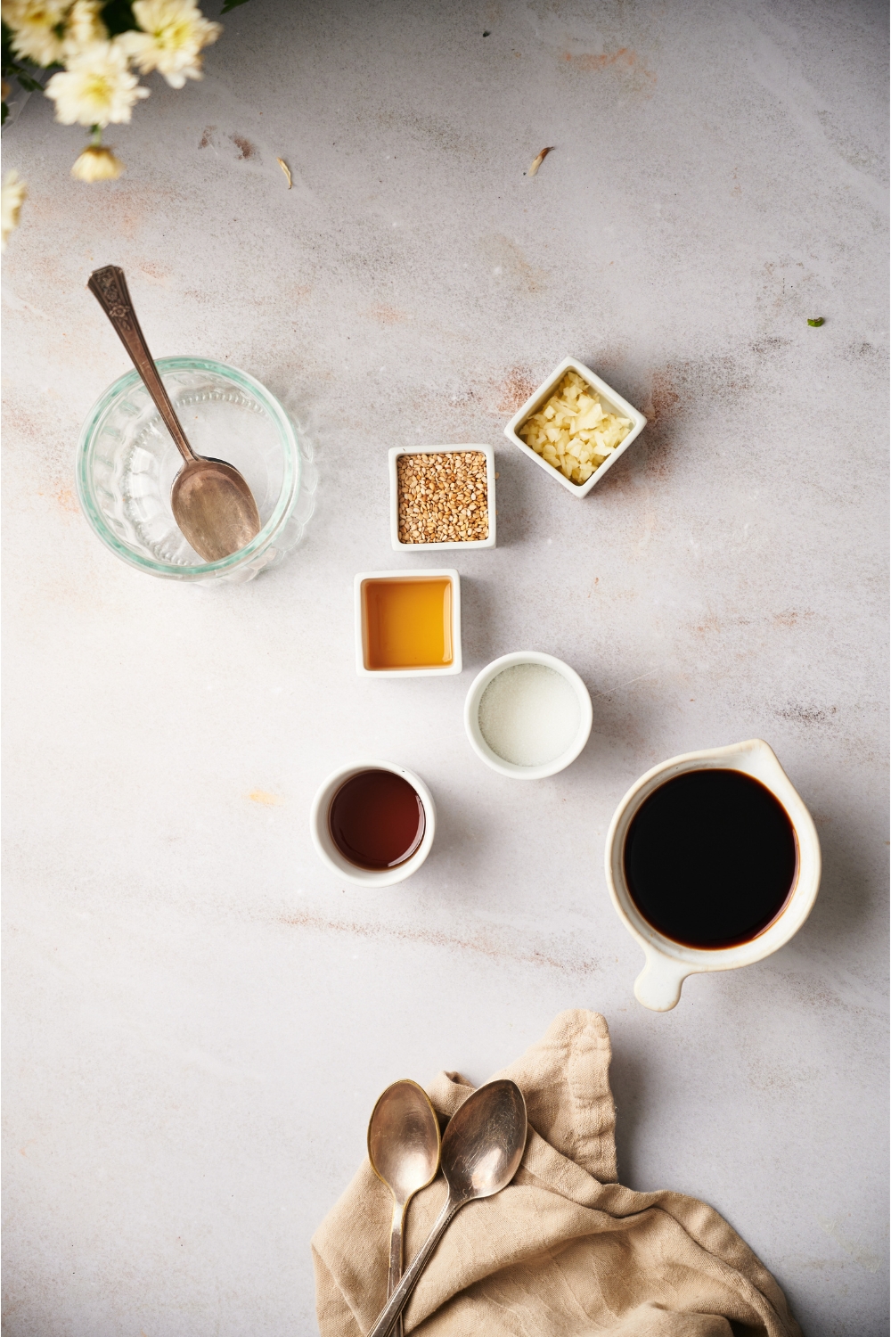 An assortment of ingredients for dumpling sauce including bowls of soy sauce, sugar, garlic, sesame seeds, sesame oil, vinegar, and an empty jar with a spoon in it.