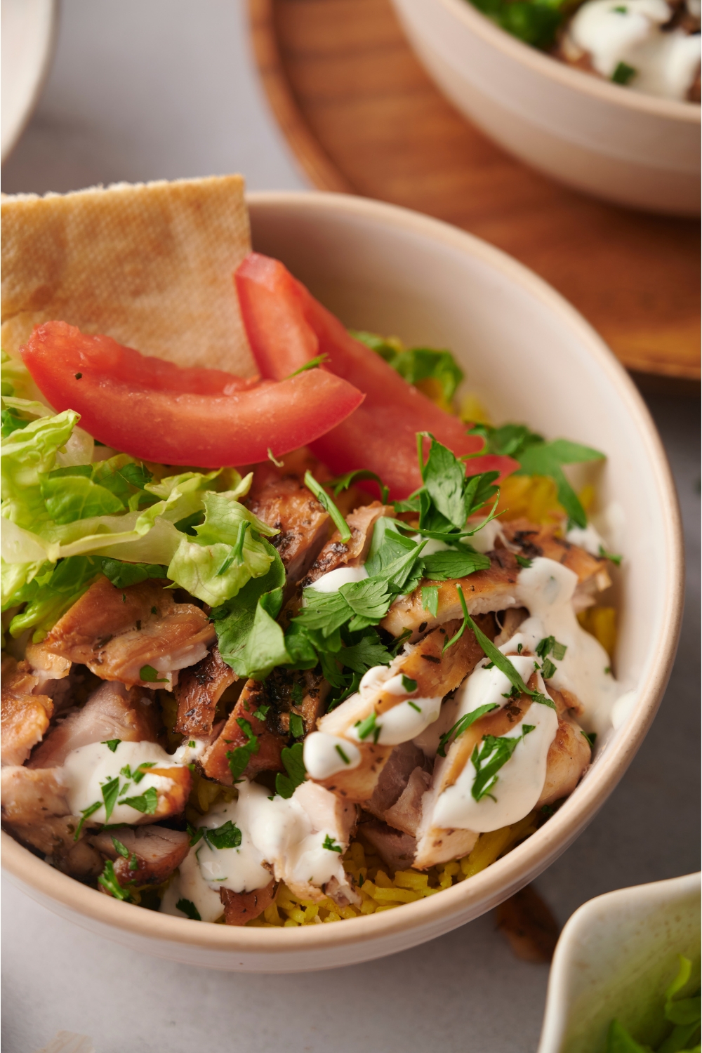 Halal chicken over rice garnished with fresh parsley, shredded lettuce, tomato, and a piece of pita bread.
