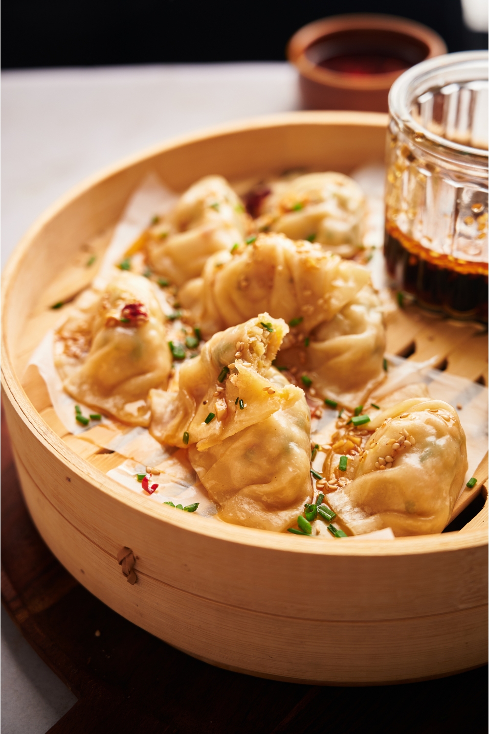 Steamed dumplings in a bamboo steamer on a wood board, garnished with green onion and sesame seeds.