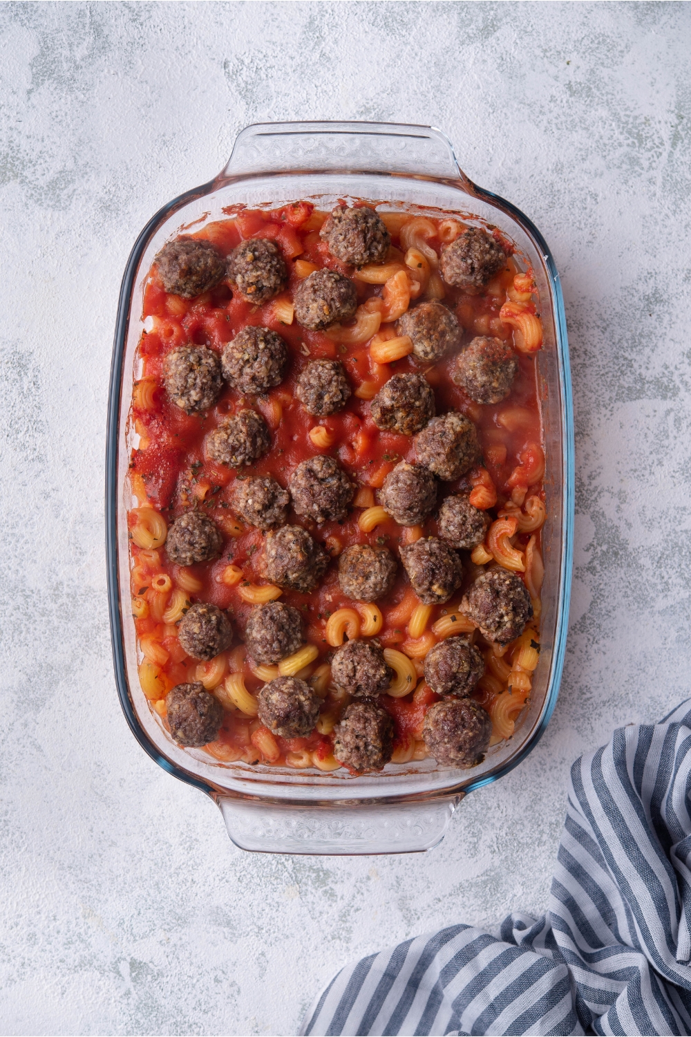 A clear baking dish filled with pasta, tomato sauce, and meatballs.
