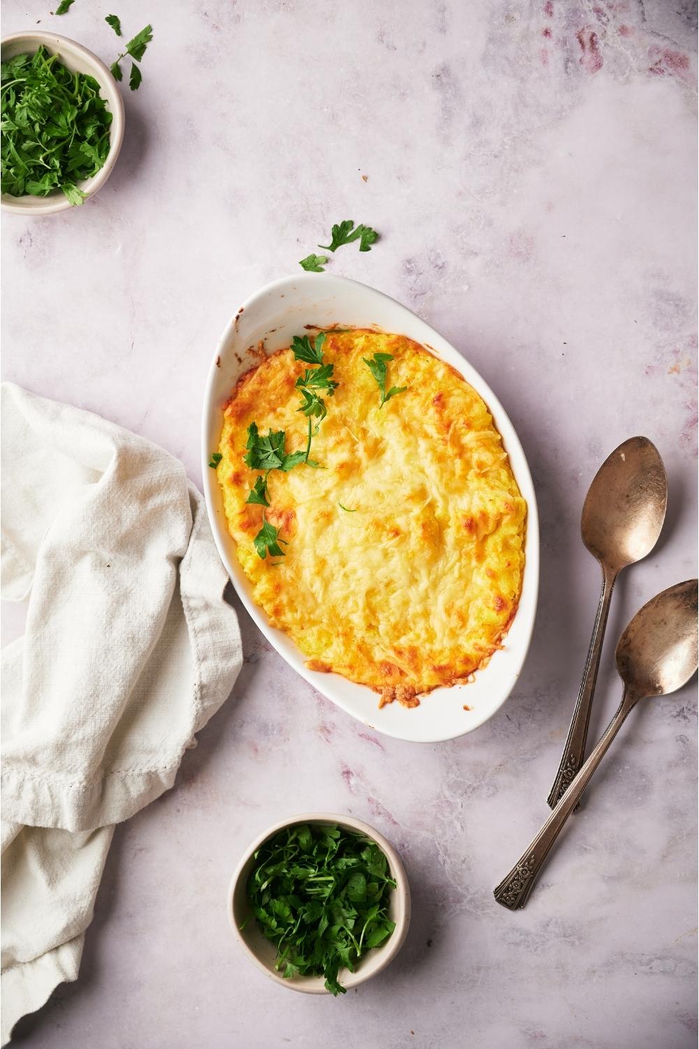 Paula Deen's corn casserole freshly baked next to two spoons and a bowl of fresh parsley