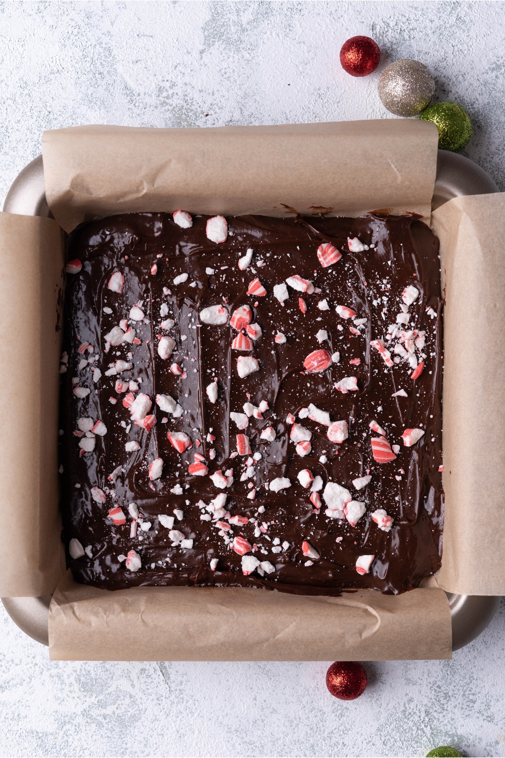 A square baking pan lined with parchment paper filled with chocolate peppermint fudge.