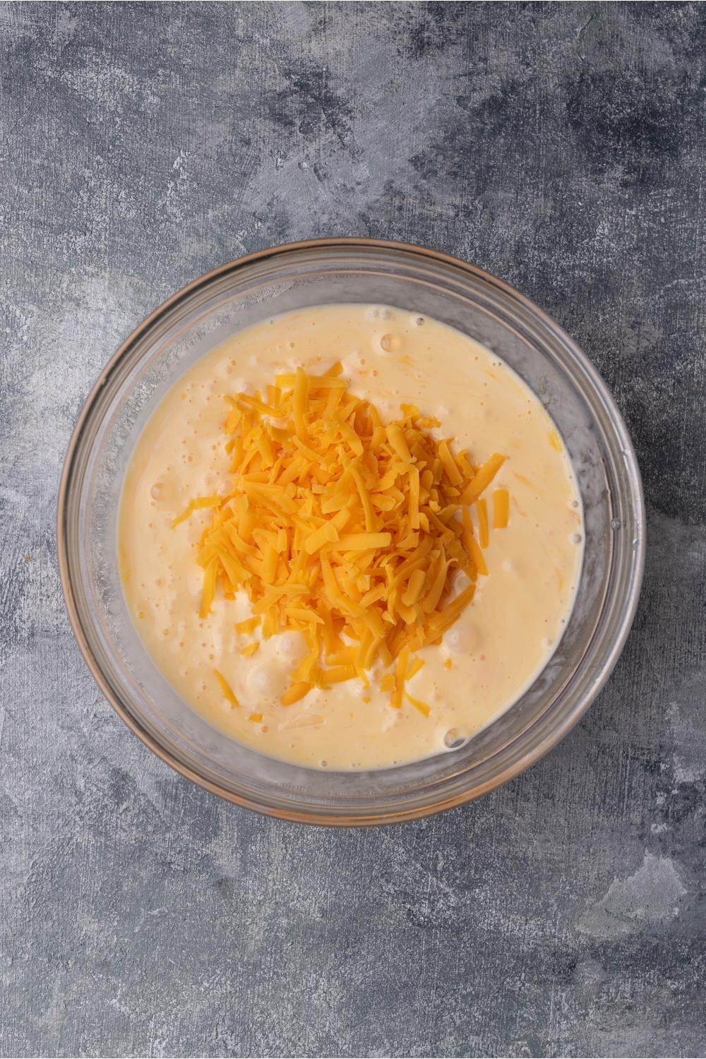 A clear bowl with beat eggs, cream, and cheese freshly added.