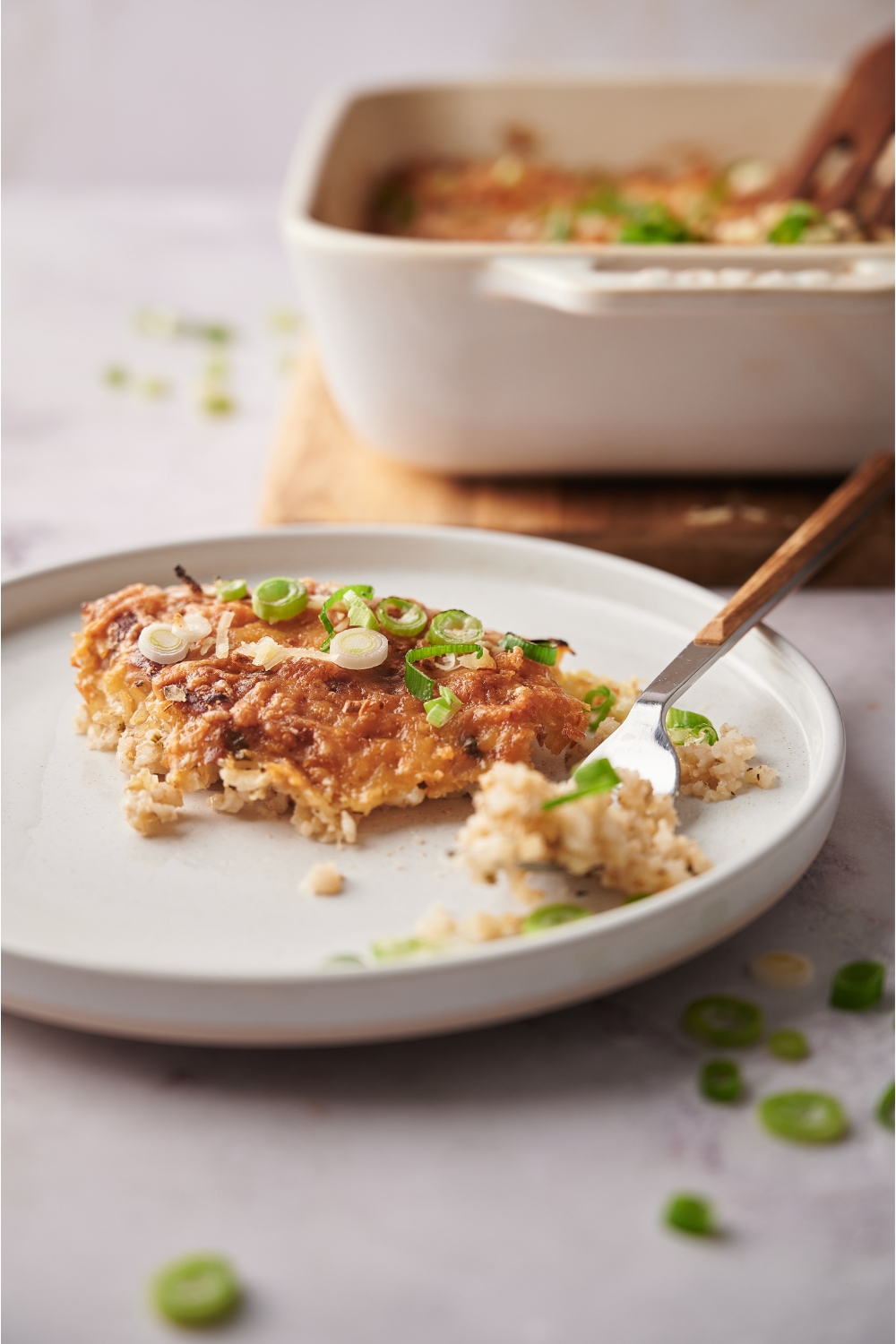 White plate with a serving of pork chop casserole and a fork on the plate. The rest of the casserole is in the background.