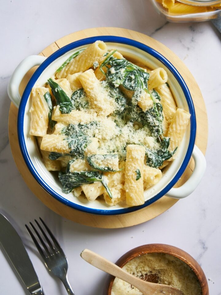 An overhead view of a bowl with spinach pasta topped with parmesan cheese. The bowl is placed on a wooden serving plate.
