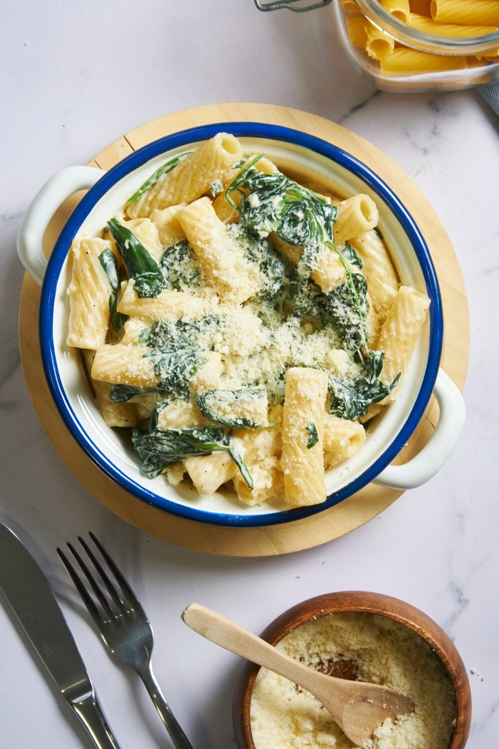 An overhead view of a bowl with spinach pasta topped with parmesan cheese. The bowl is placed on a wooden serving plate.