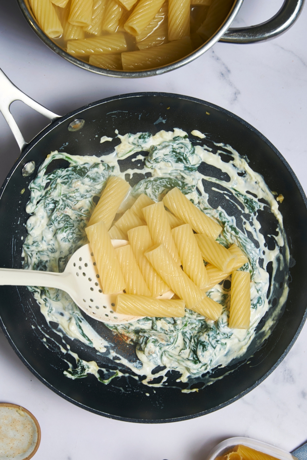 A pan with spinach pasta sauce in it. Cooked pasta has just been added to it.