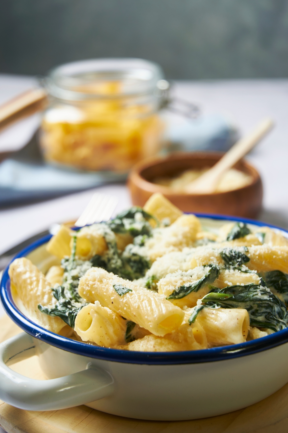 A bowl with spinach pasta topped with parmesan cheese. The bowl is placed on a wooden serving plate.