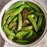 An overhead view of a small bowl with butter snap peas.