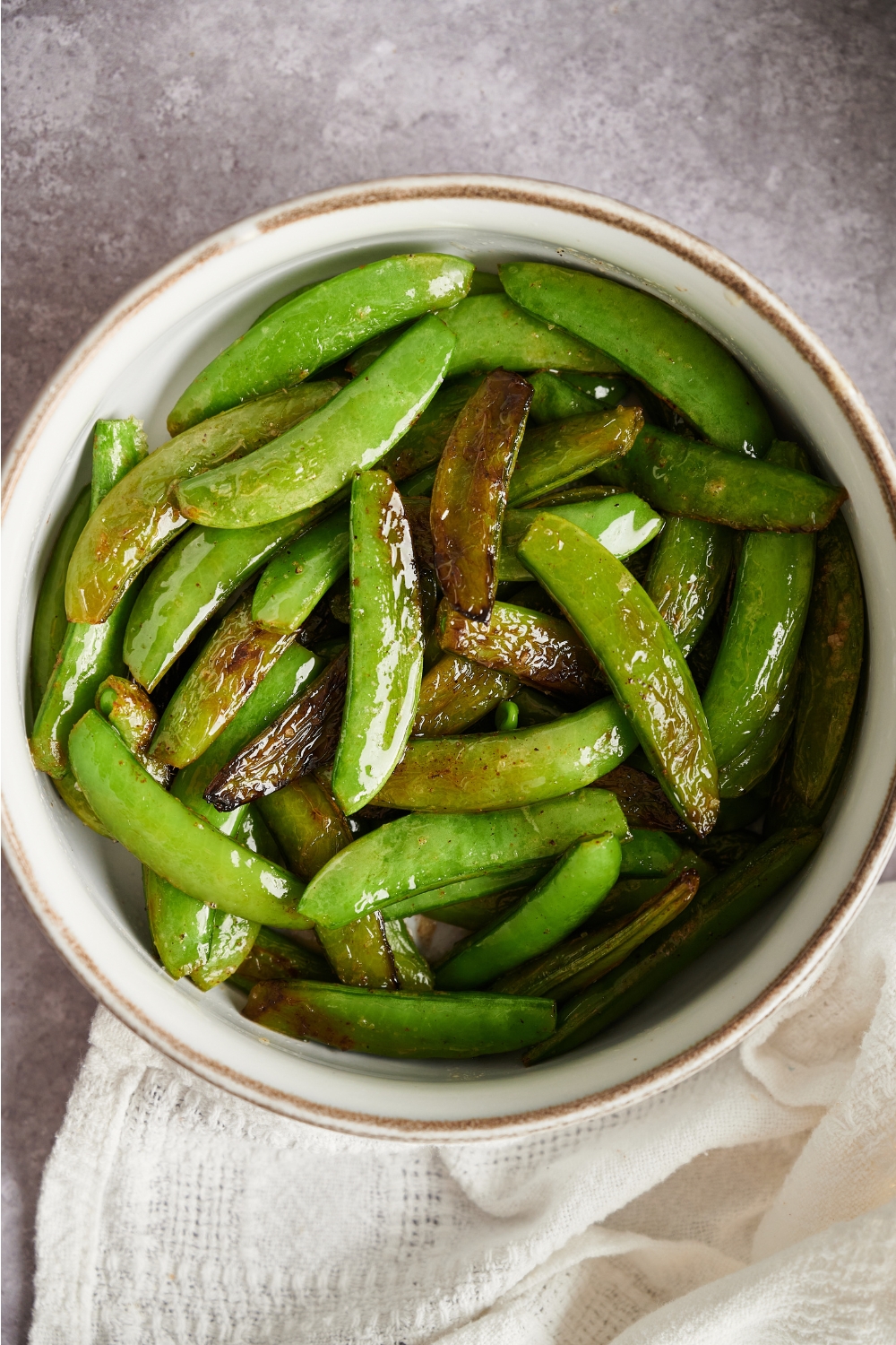 An overhead view of a small bowl with butter snap peas.