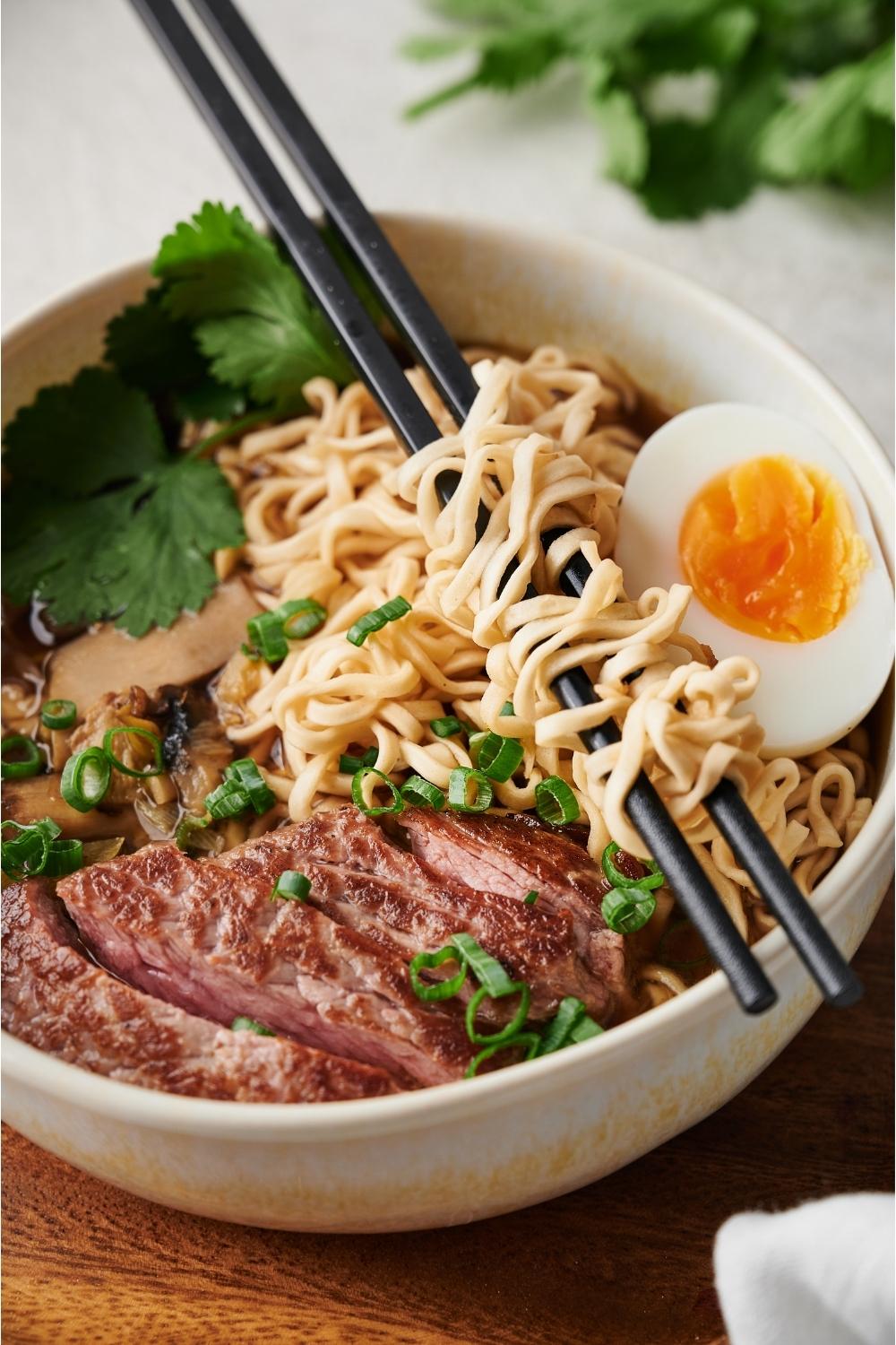beef ramen in a white bowl on a wood plate with chopsticks resting on the bowl