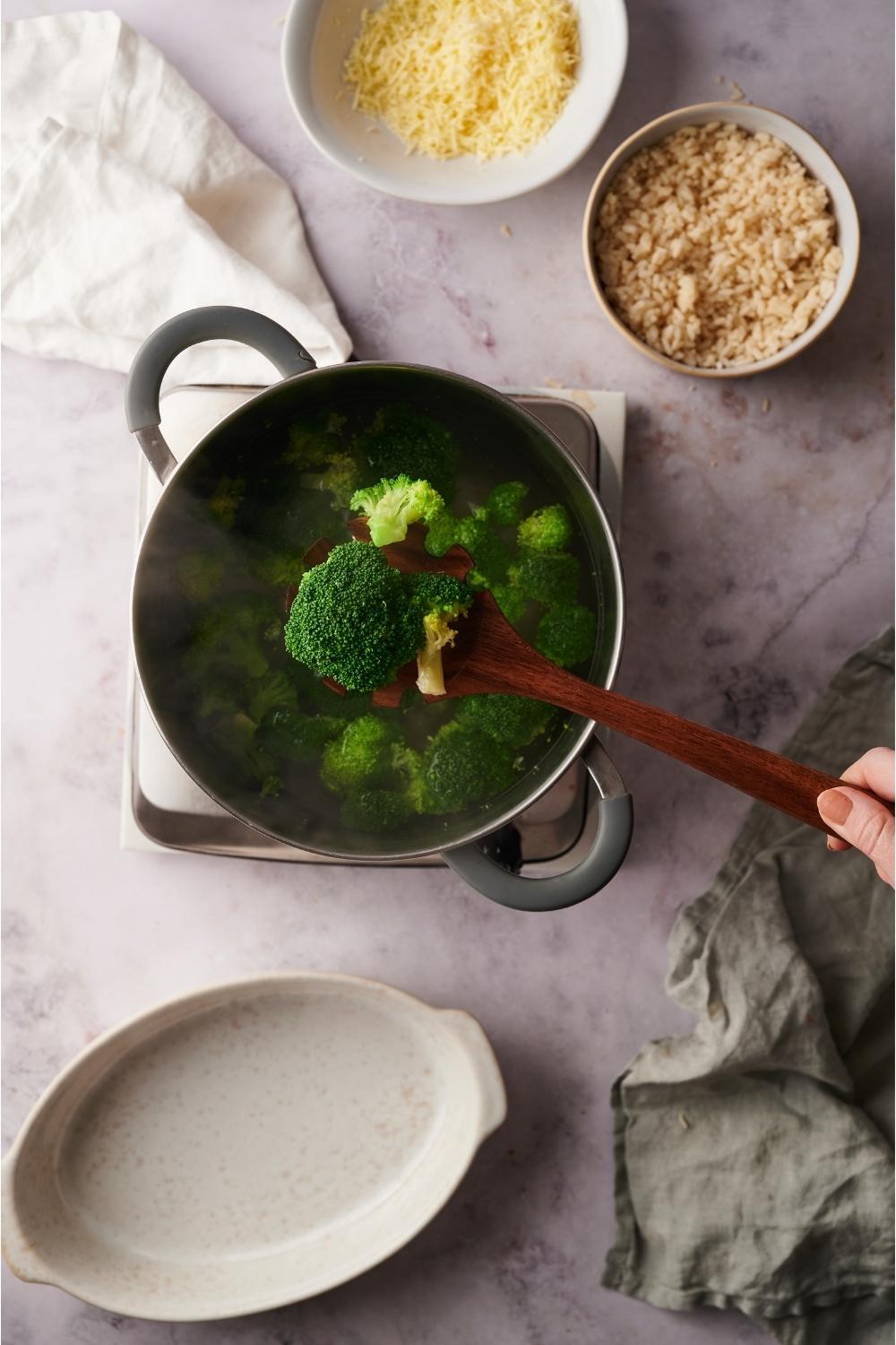 Pot of broccoli freshly steamed with a person removing the cooked broccoli from the pot with a wooden spoon.