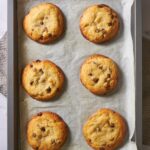 Six baked cookies in two rows of three on top of a baking sheet lined with parchment paper.
