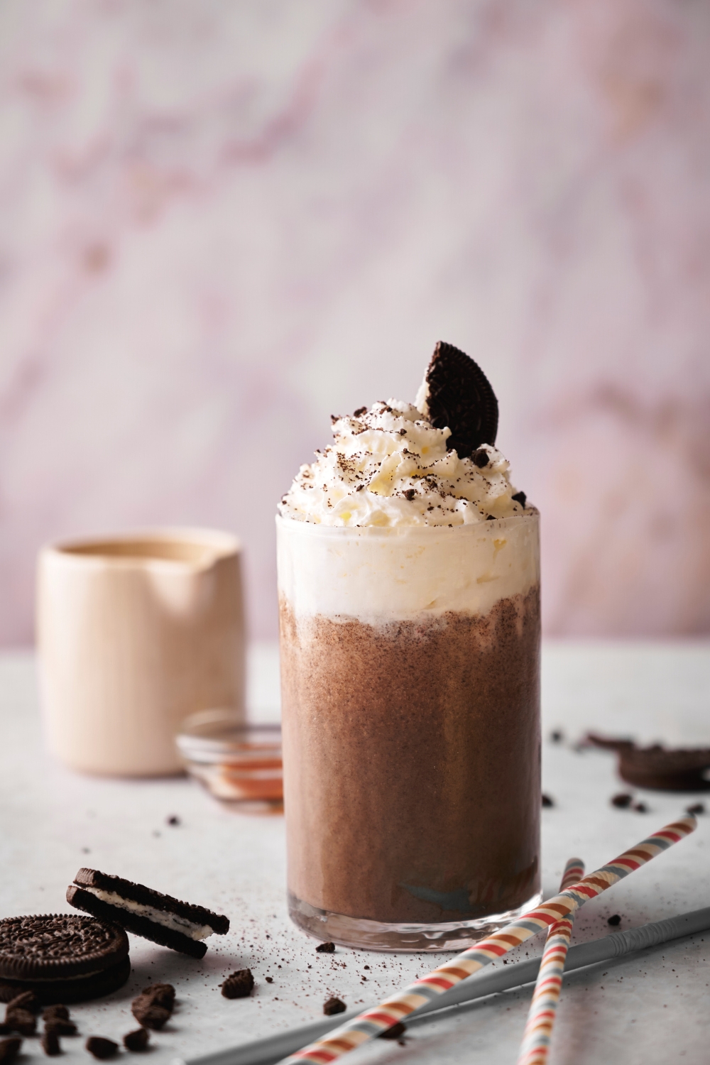 A glass that is filled with an Oreo milkshake with whipped cream on top.