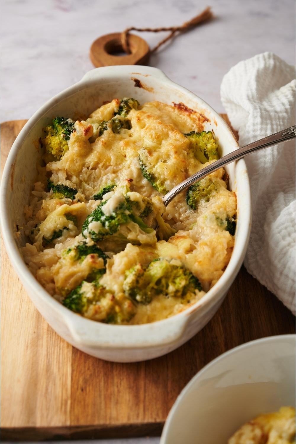 Broccoli rice casserole in a casserole dish on a wood board with a spoon in the dish.
