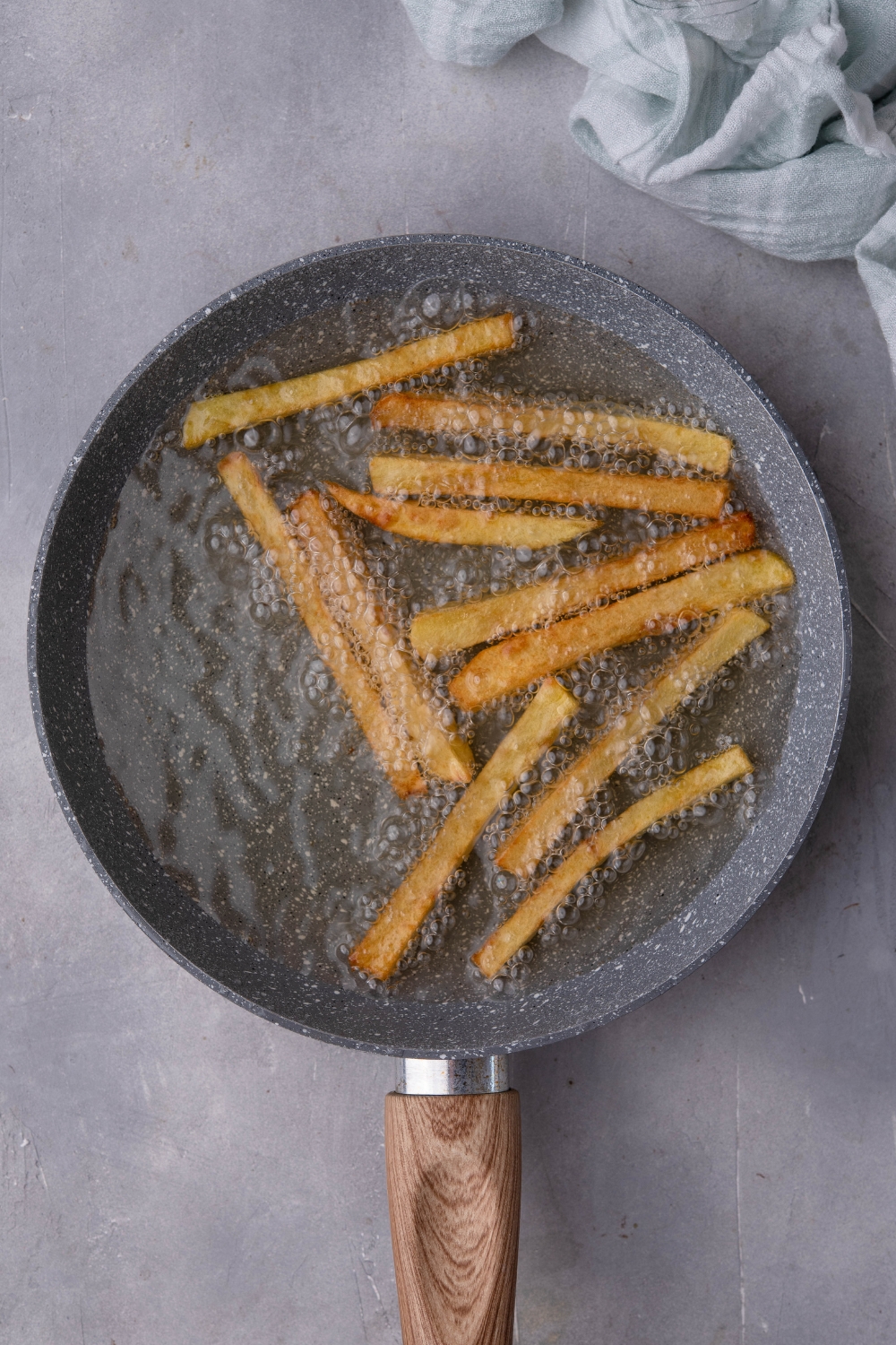 A pan of hot oil with a single layer of cut fries refrying.