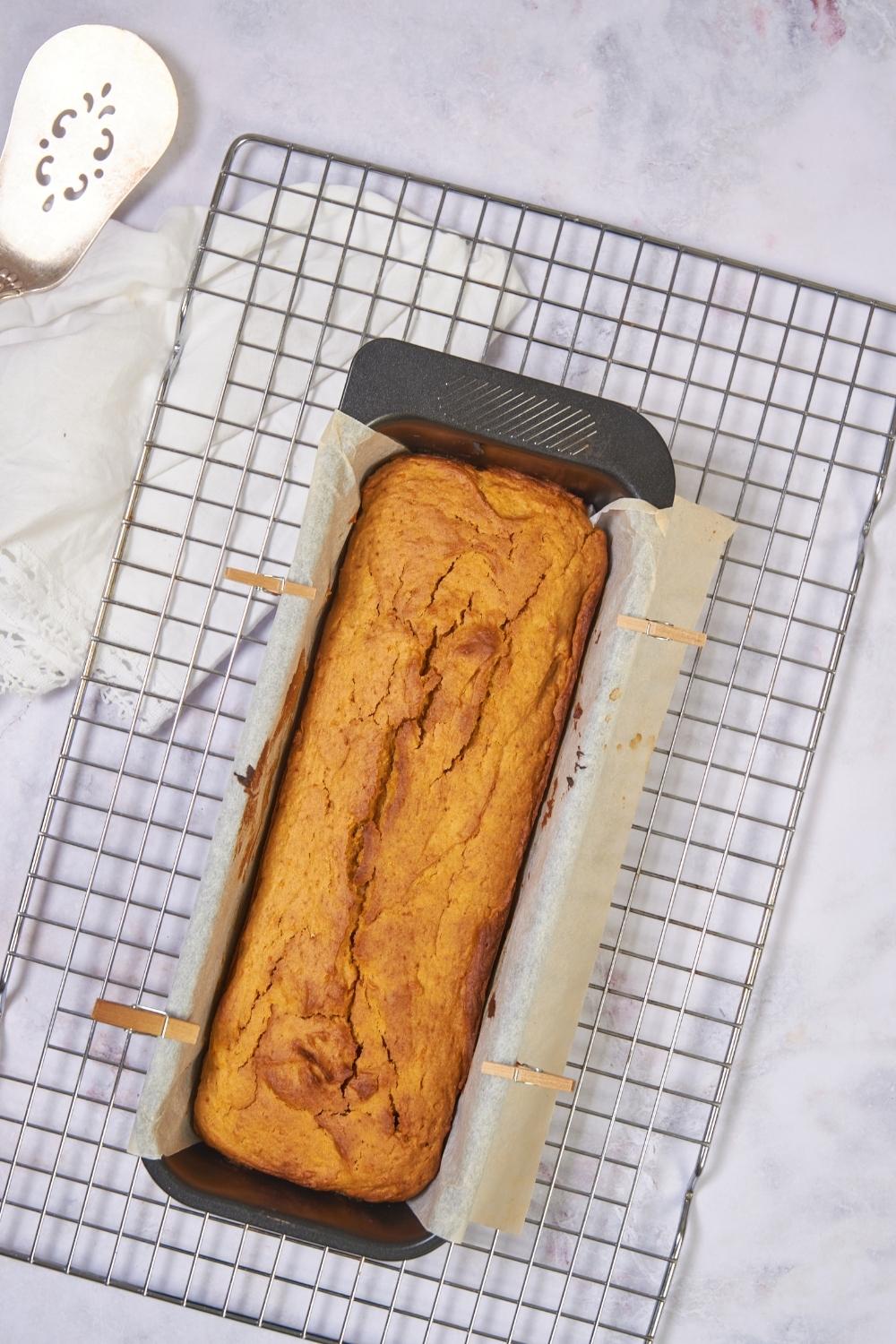 Freshly baked sweet potato bread in a loaf pan lined with parchment paper on a cooling rack.