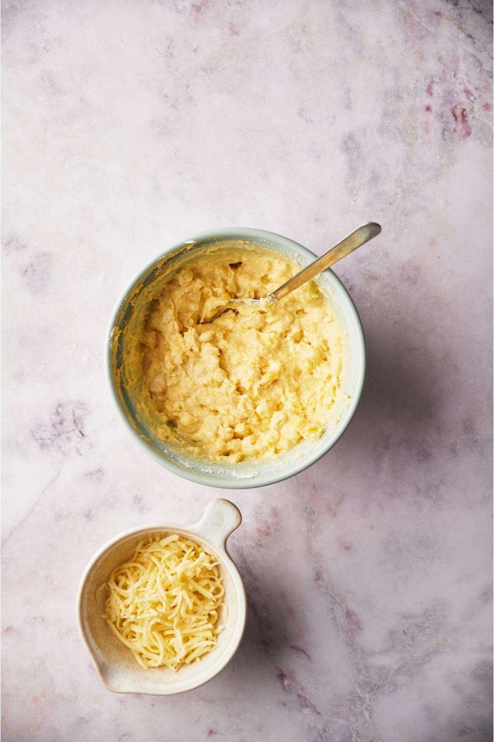 Blue bowl with corn casserole batter next to a small bowl of shredded cheese