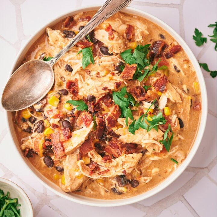 A spoon line across shredded chicken, bacon, corn, and beans in a white ball that is filled with creamy chili.