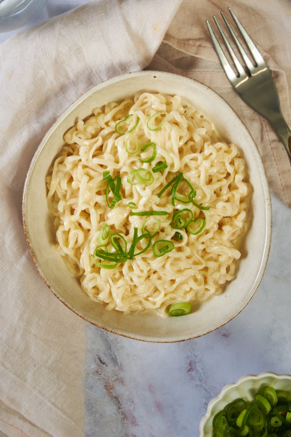 Green scallions on top of ramen noodles that are in a white bowl on a counter.