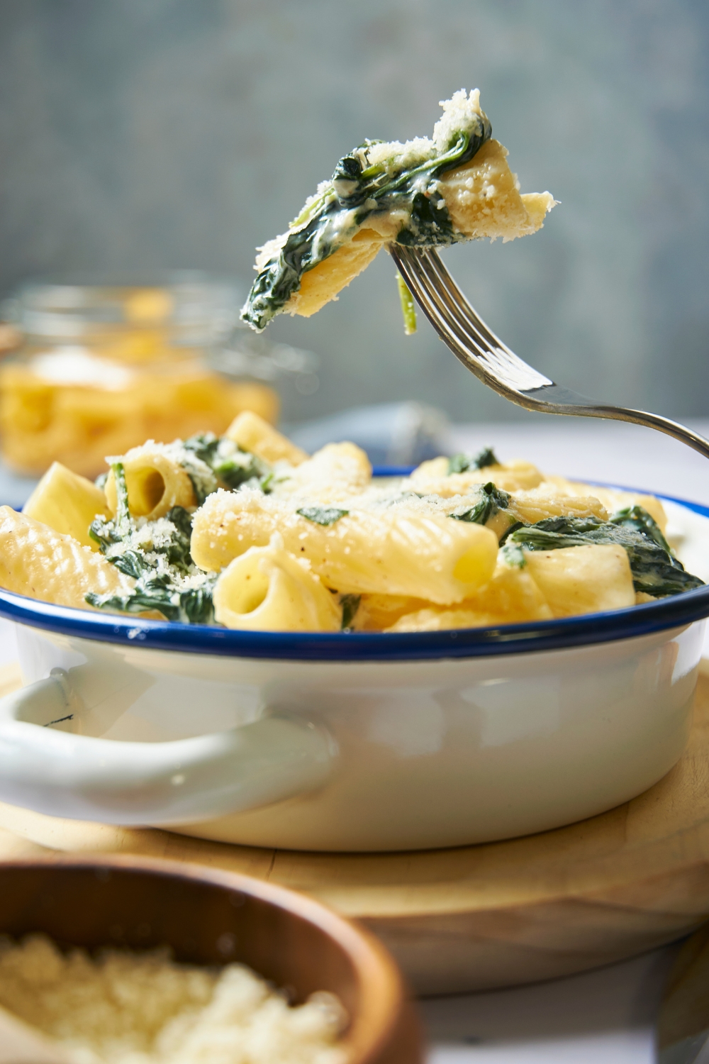 A bowl with spinach pasta topped with parmesan cheese. A fork is lifting a scoop of the spinach pasta above the bowl.