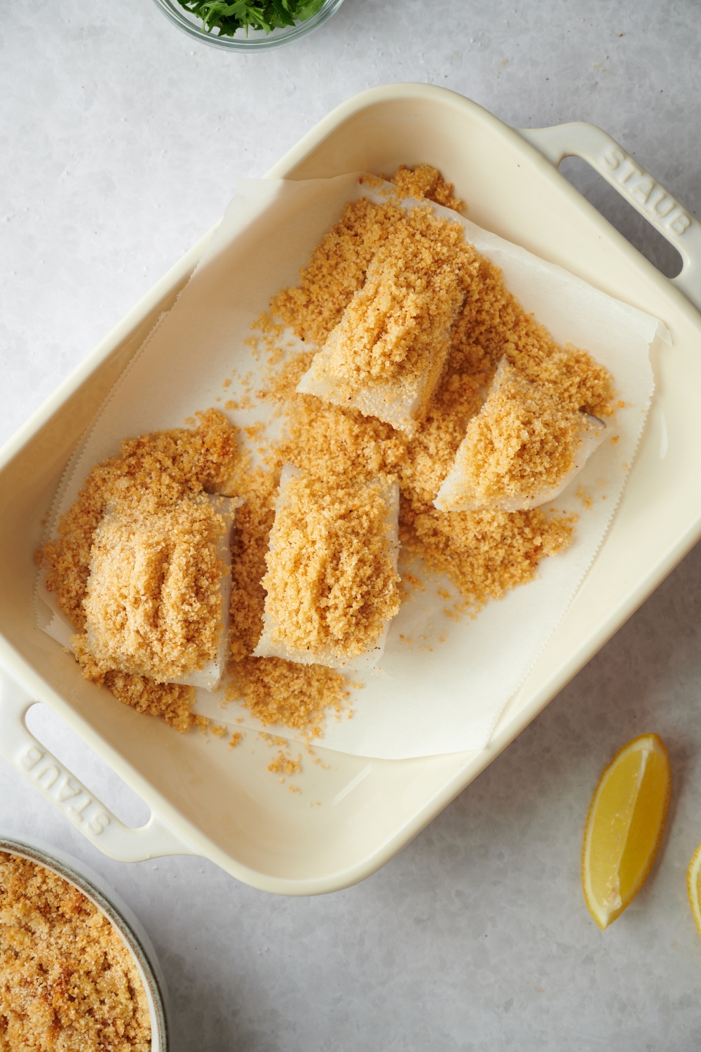 A bread crumb mixture on top of four haddock fillets on a sheet of parchment paper in a baking dish.