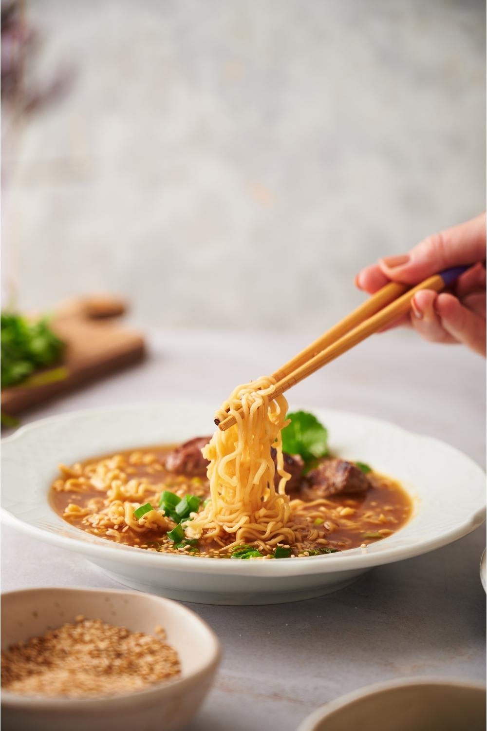 Hand using chopsticks to grab ramen noodles from a bowl