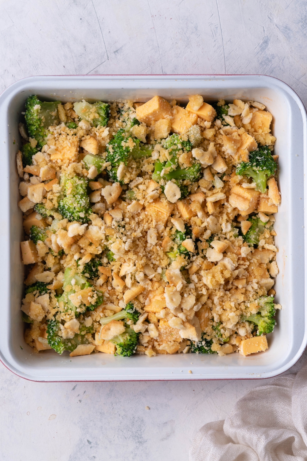 An overhead view of a casserole dish with broccoli, cubed cheese, and crumbled crackers.