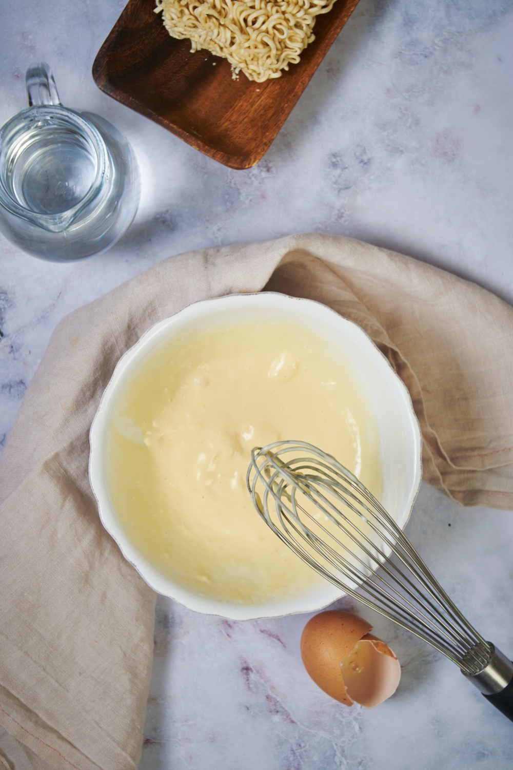 A whisk hovering over a bowl that has a white creamy sauce in it.