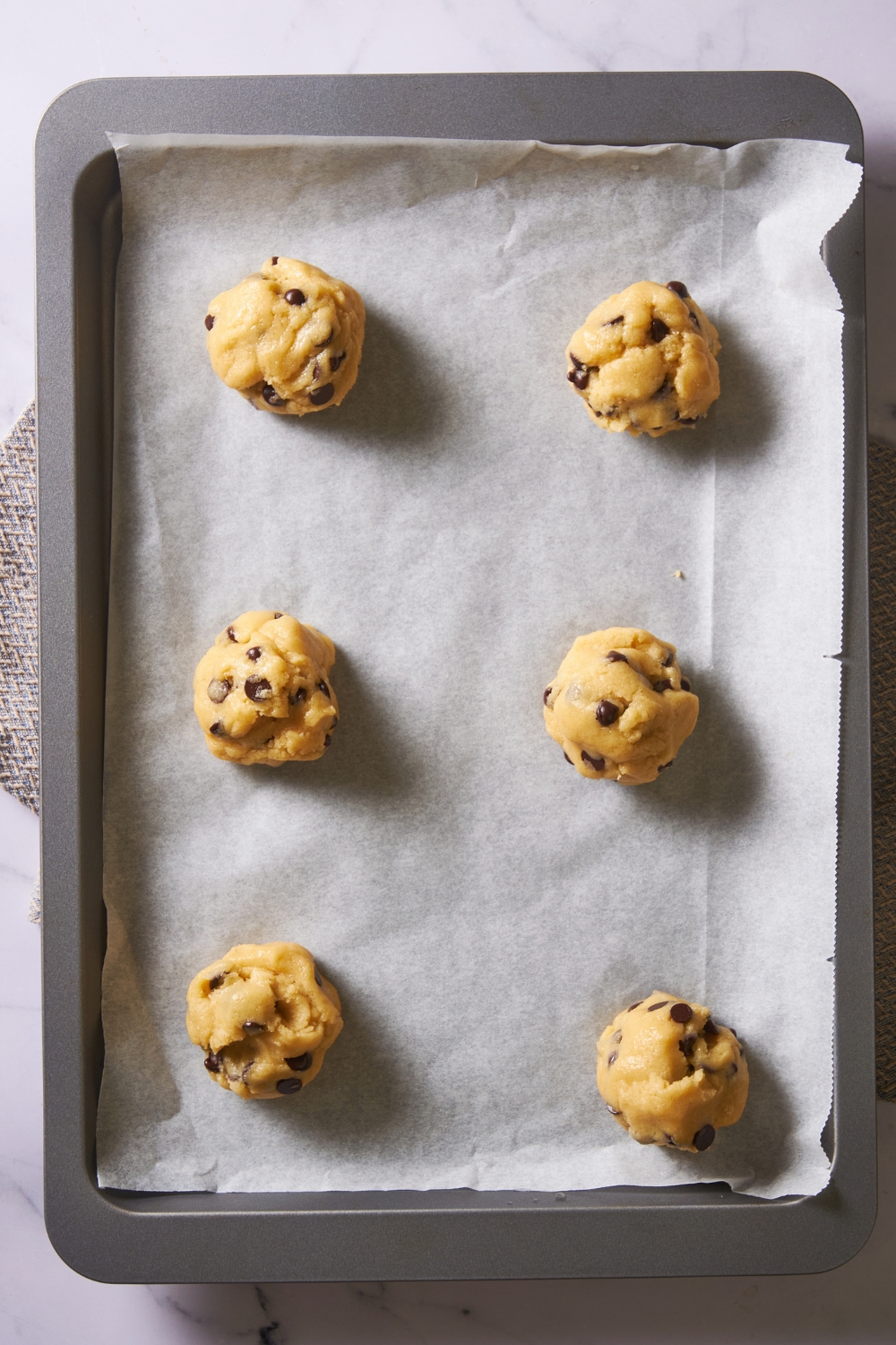 Six cookie dough balls on a baking sheet lined with parchment paper.
