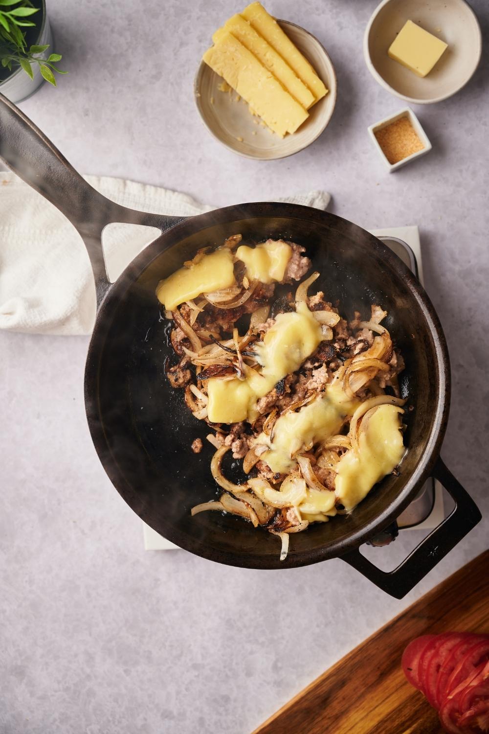 Melted cheese on top of ground beef and caramelized onions in a skillet.