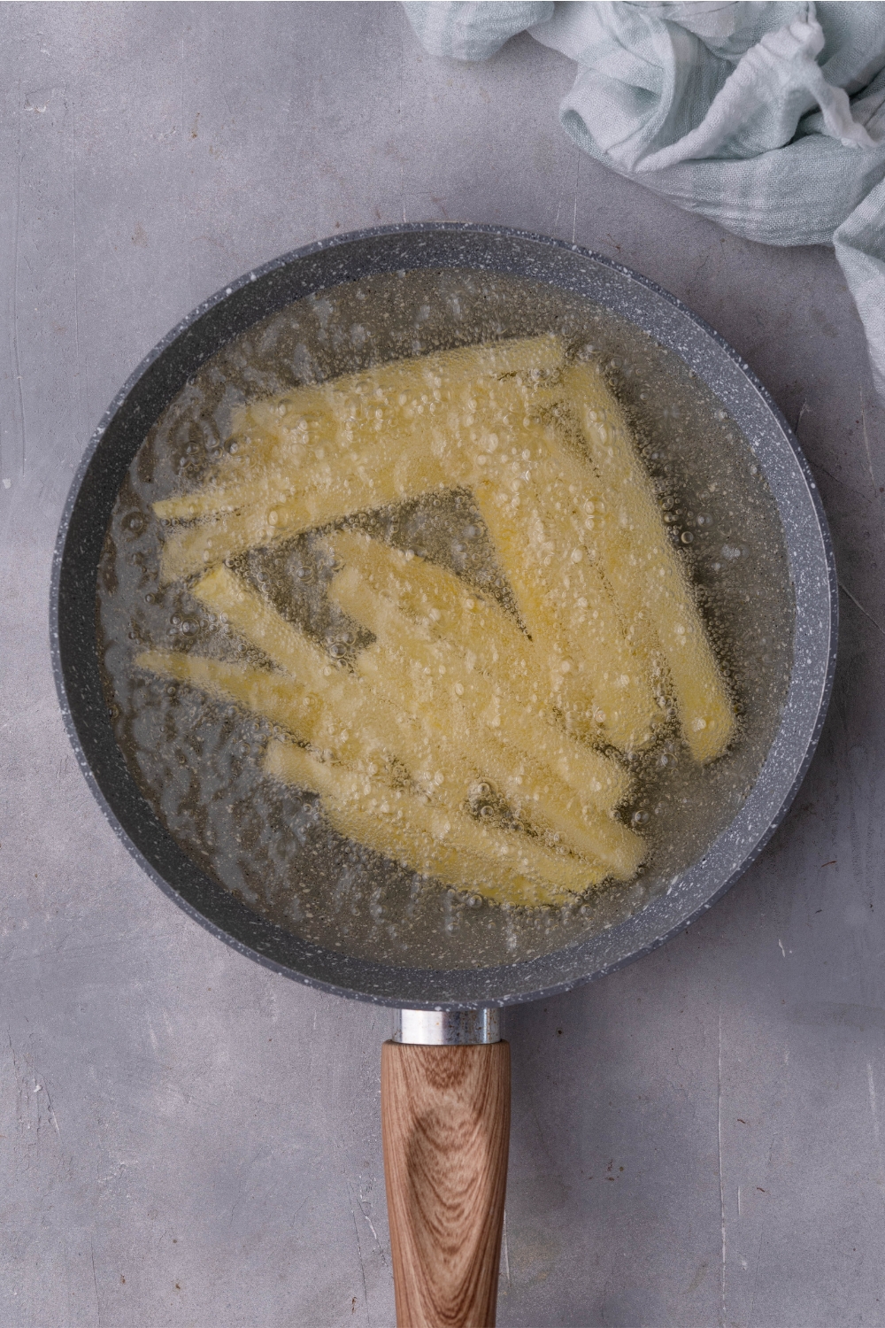 A pan of hot oil with a single layer of cut fries frying.