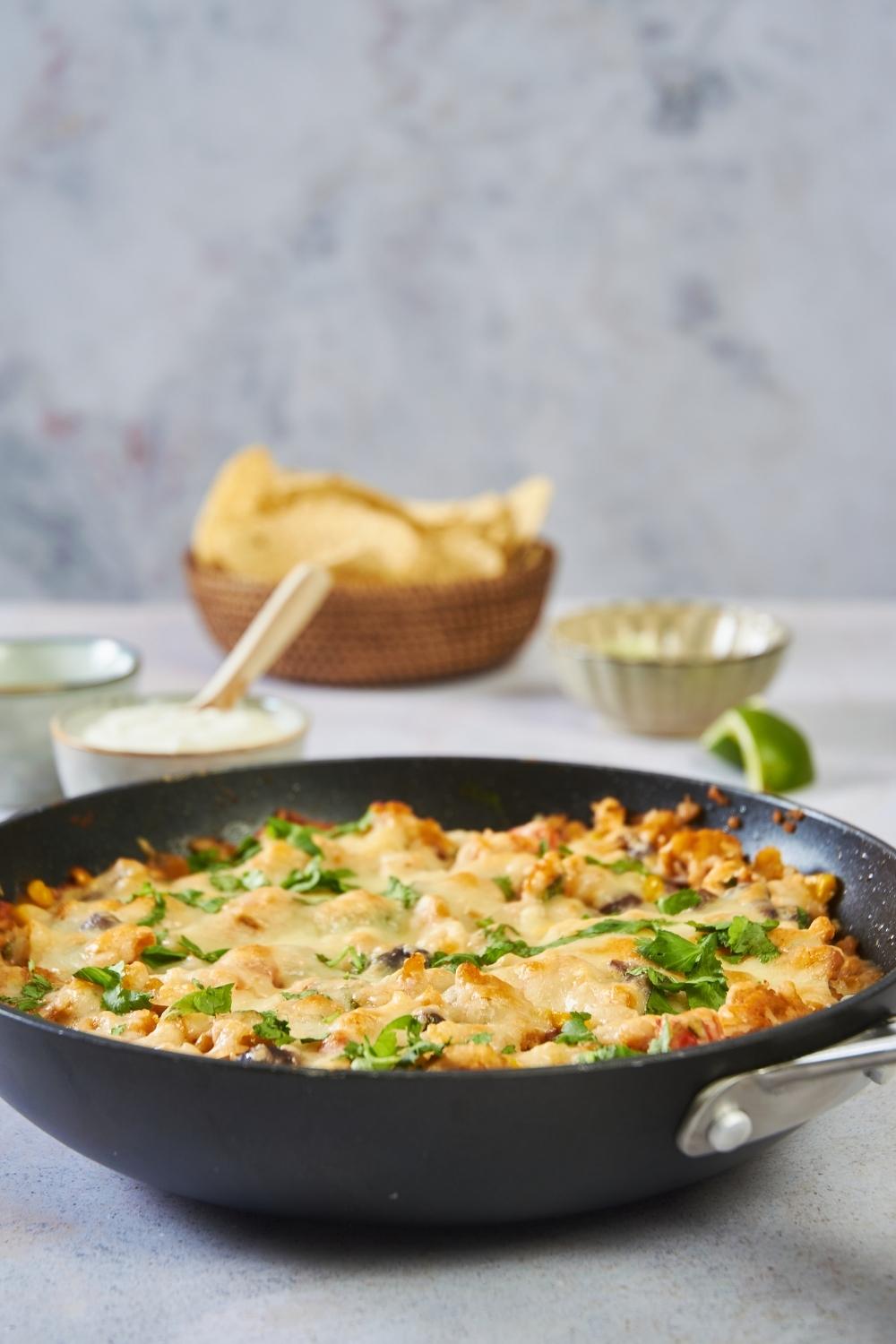 A black skillet filled with ground turkey, melted cheese, and cilantro. There are other topping ingredients in the background.