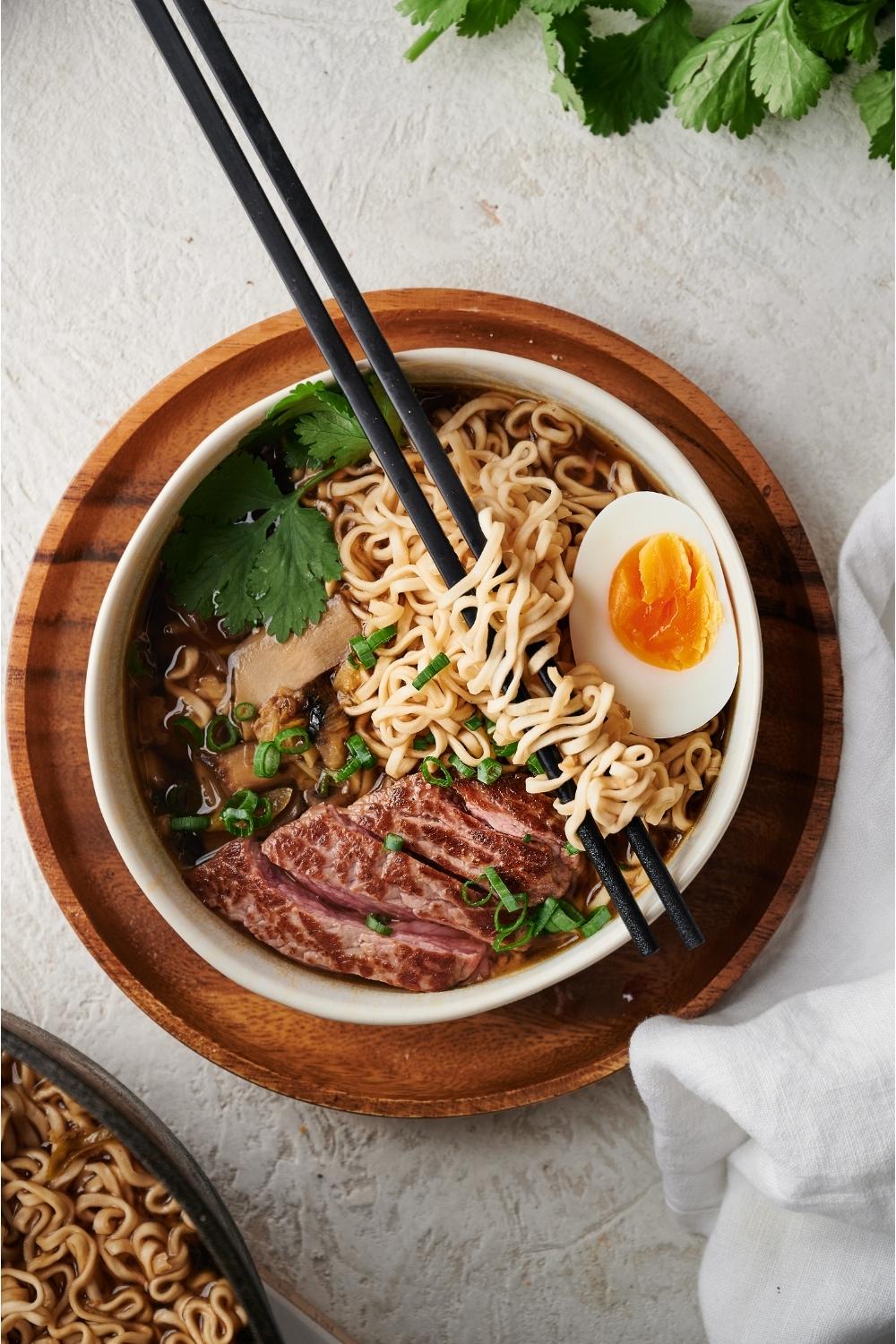 beef ramen in a white bowl on a wood plate with chopsticks resting on the bowl