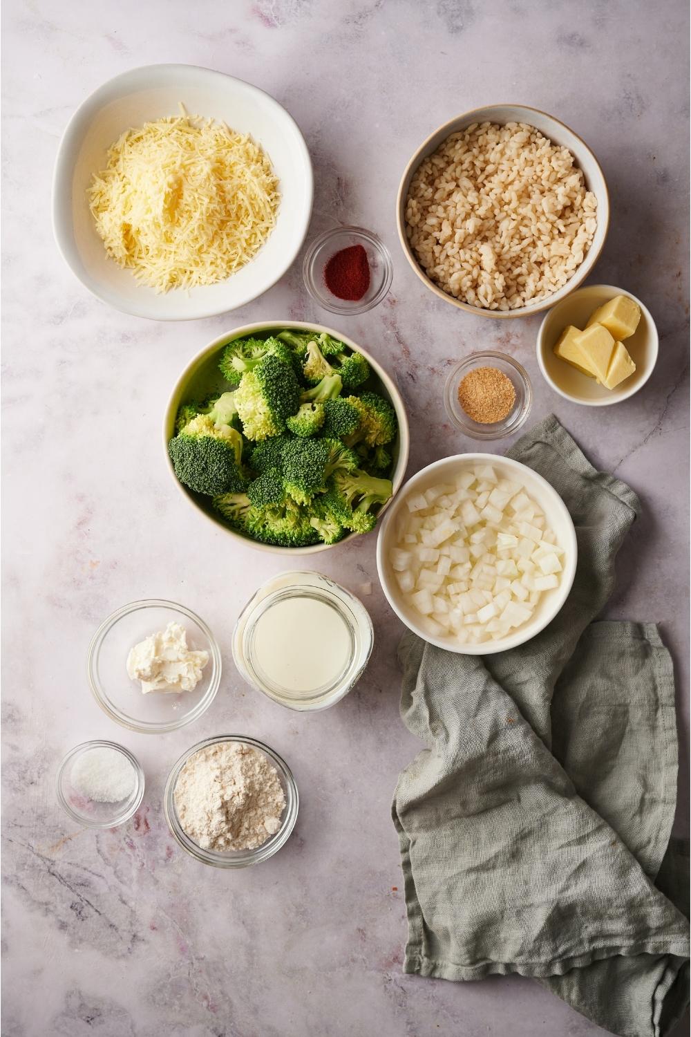 An assortment of ingredients for broccoli rice casserole including bowls of broccoli, rice, cheese, milk, onions, butter, and spices.
